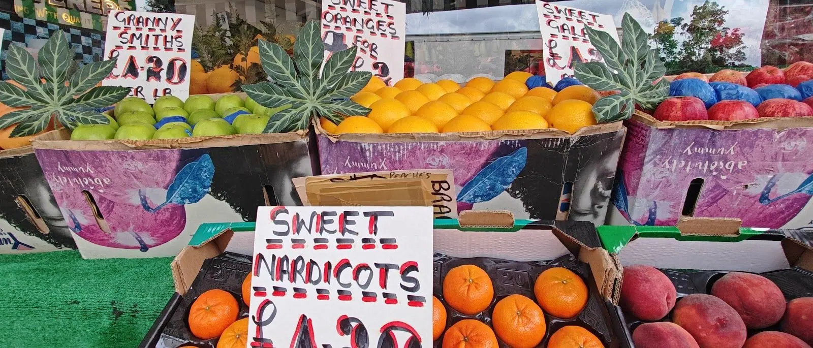 Crates of apples, oranges and apricots with hand-written price cards at Parade Fruiterers, West Ealing